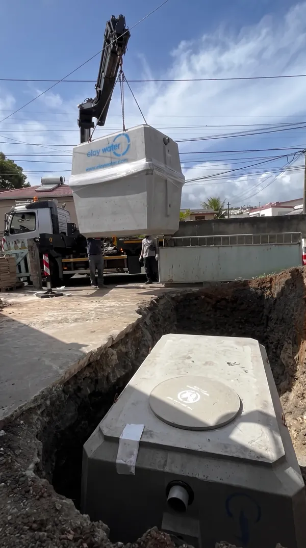 Grue déchargeant une cuve de filtration en béton Eloy Water dans une fosse d'assainissement.