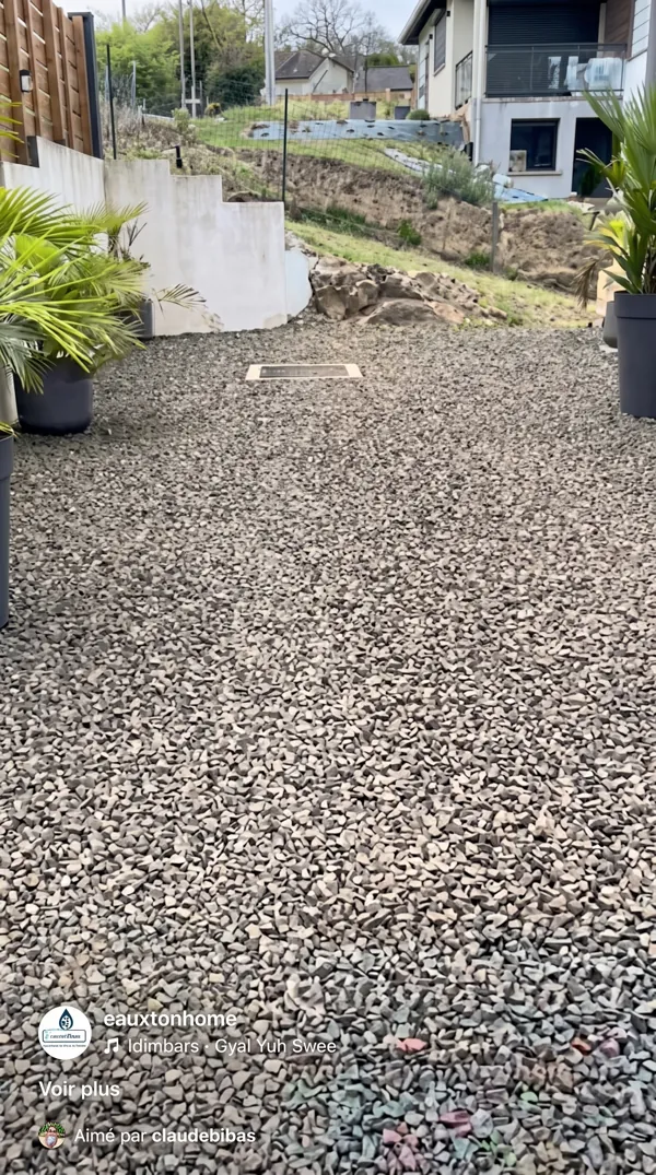 Trappe d'accès d'une citerne en béton enterrée sous un sol en gravier.