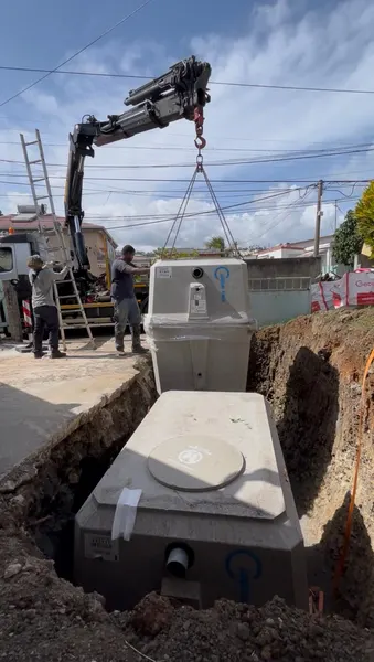 La cuve suspendue à la grue, deux techniciens la guident dans la fouille.
